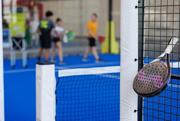 Raquette de padel au premier plan, joueurs flous sur le terrain bleu derrière à Salbris en Loir-et-Cher 41