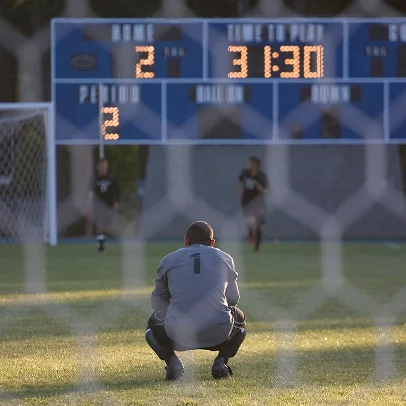 Gardien de but accroupi sur un terrain de soccer, tableau de score en arrière-plan à Salbris en Loir-et-Cher 41