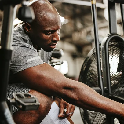 Homme transpirant ajustant un vélo d'exercice, lisant des notes dans une salle de sport à Salbris en Loir-et-Cher 41