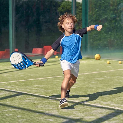Jeune garçon aux cheveux bouclés jouant au padel, frappant une balle sur le court à Salbris en Loir-et-Cher 41