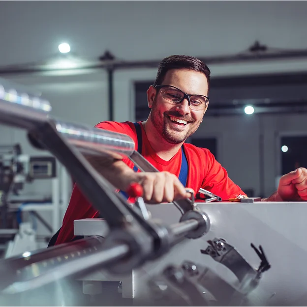 Opérateur souriant en t-shirt rouge et salopette bleue, travaillant sur une machine à Salbris en Loir-et-Cher 41